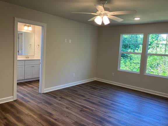 A room with a ceiling fan and a window overlooking greenery.