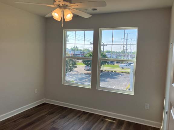 A room with a ceiling fan and two windows overlooking a parking lot.