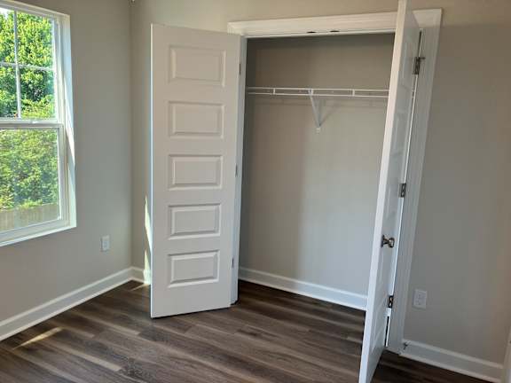 A white door is open to a room with a white wall and a wooden floor.