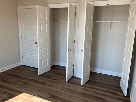 A room with three white doors and wood flooring.