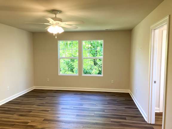 A room with a ceiling fan and a window with a view of trees.