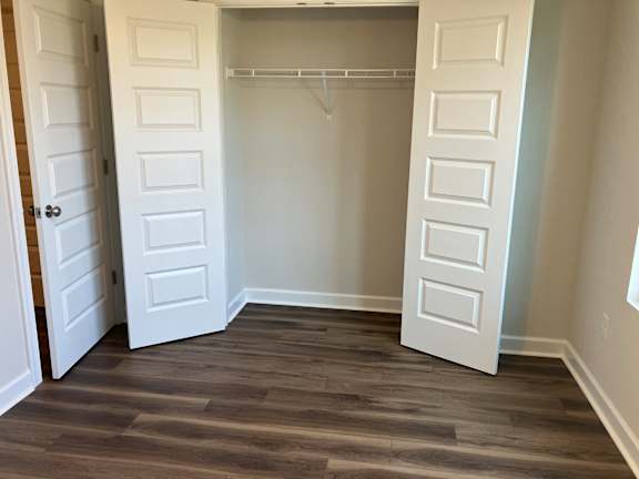 A white closet with a wooden floor and a white door.
