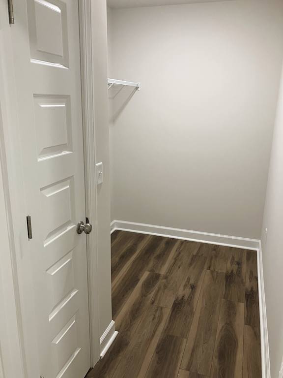 A white door with a silver handle is open to a hallway with wood flooring.