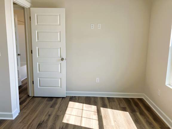 A white door is in a room with wood flooring and a window letting in sunlight.