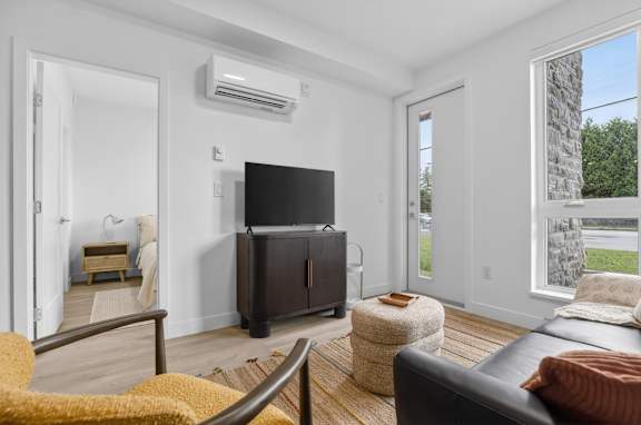 A living room with a black leather couch, a yellow chair, and a flat screen TV mounted on the wall.
