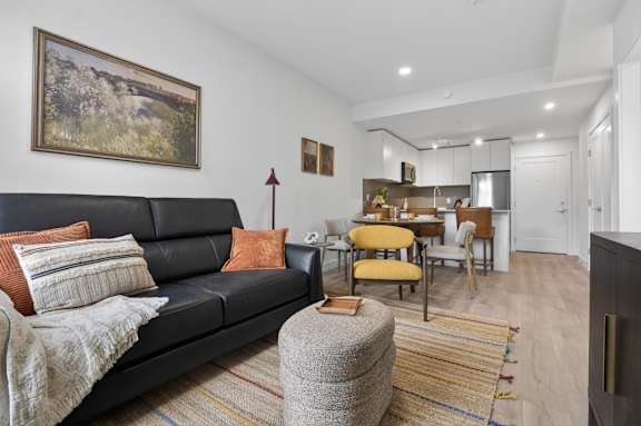 A living room with a black couch and a painting on the wall.