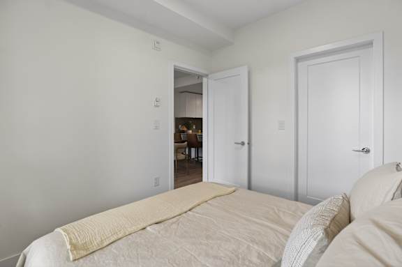 A bedroom with a bed in the foreground and a dining area in the background.