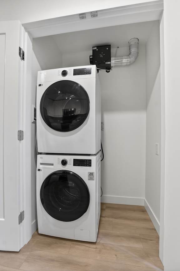 A white dryer and washer are stacked on top of each other in a small, white-walled laundry room.