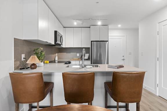 A modern kitchen with brown leather chairs and a white countertop.
