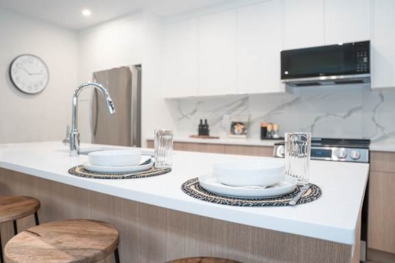 A modern kitchen with a white countertop and a clock on the wall.