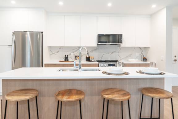 A modern kitchen with a white countertop and wooden stools.