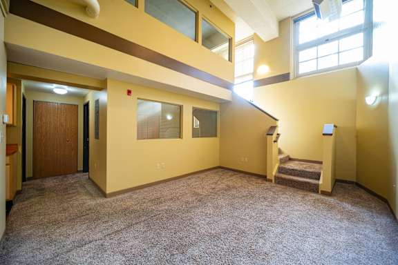 A carpeted room with a staircase leading to another room.