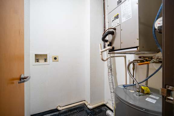 A room with a door, a wall-mounted unit with a hose connected to it, and a yellow tag on the unit.