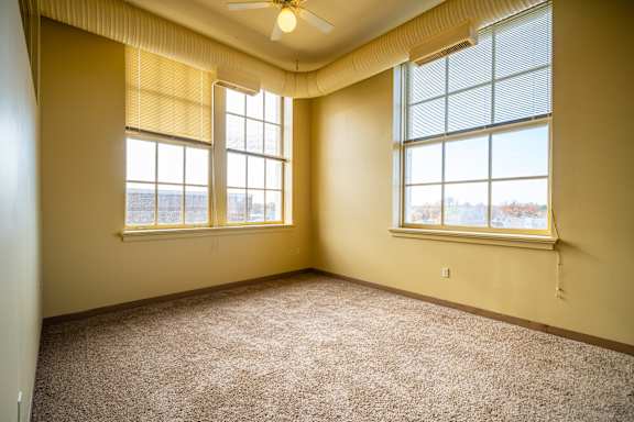 A room with a carpeted floor and two windows.