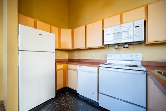 A white refrigerator stands in a kitchen with a white stove and dishwasher.