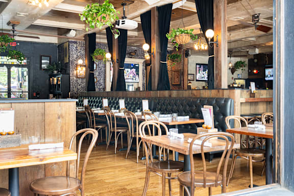 A restaurant with wooden tables and chairs and hanging plants.