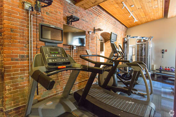 A treadmill with a control panel on top is in a room with brick walls.