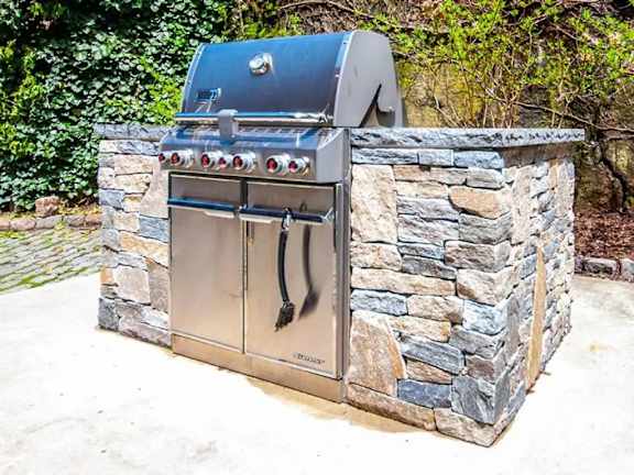 A charcoal grill is built into a stone wall.