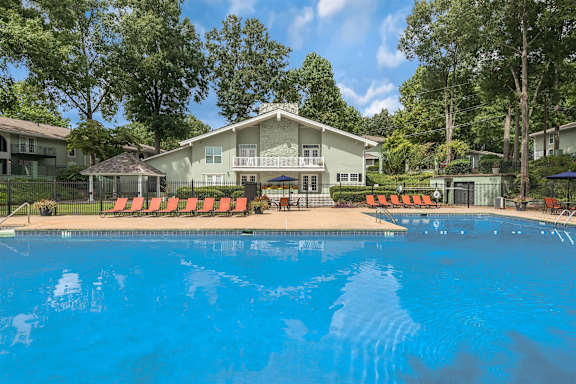 A swimming pool in front of a house with orange lounge chairs.