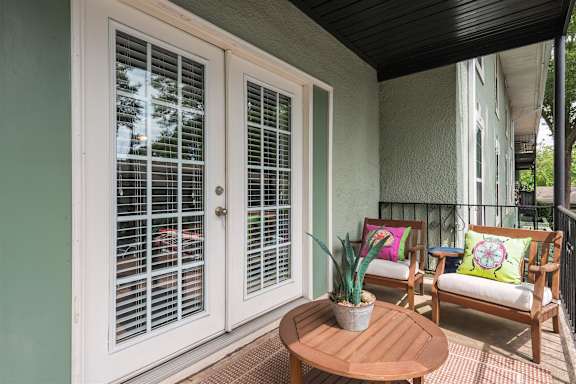 A patio with a table, two chairs and a potted plant.