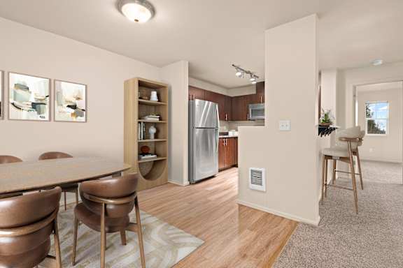 A kitchen with a refrigerator, dining table and chairs.