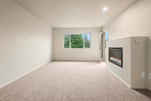 A spacious room with a carpeted floor and a window showing greenery outside.