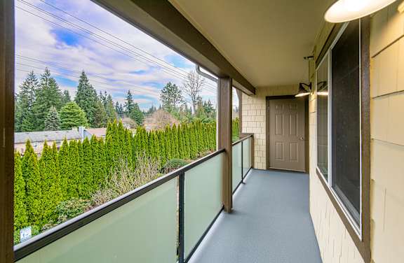 A balcony with a glass railing overlooking a green hedge.