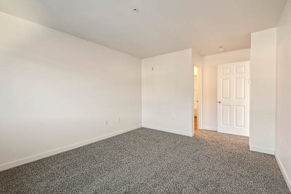 A room with a carpeted floor and a door on the right side.