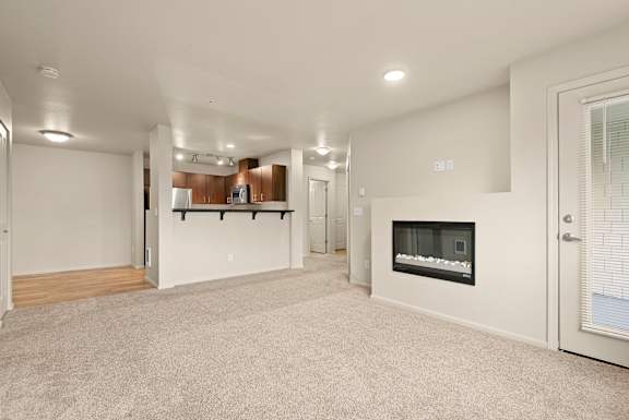 A spacious living room with a fireplace and a kitchen area in the background.