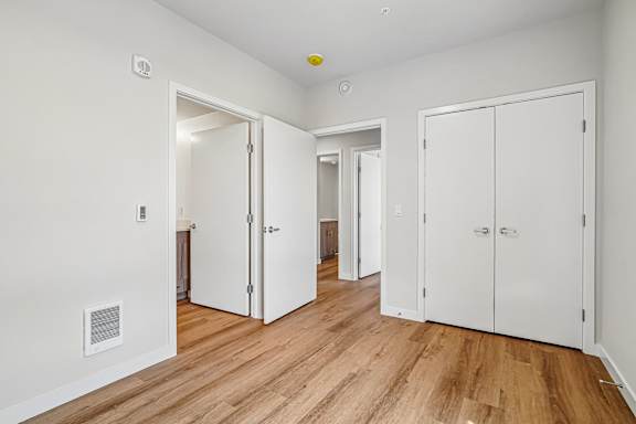 A room with white walls and wooden floors has two white doors and a small window.