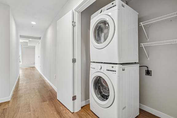 A white washing machine is stacked on top of another white washing machine in a room with white walls.