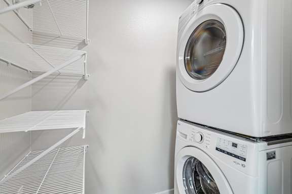 A white washing machine is stacked on top of a white dryer in a laundry room.