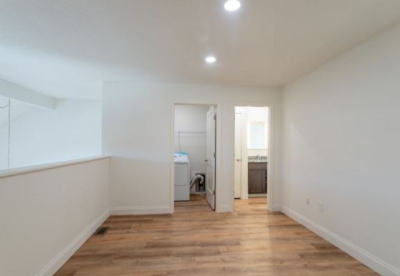 A room with white walls and wooden floors, with a washing machine and dryer in the corner.