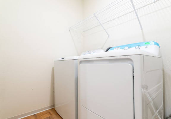 A white washing machine with a blue control panel is in a room with a white wall.