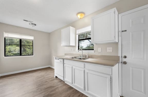 A kitchen with white cabinets and a window overlooking a green landscape.