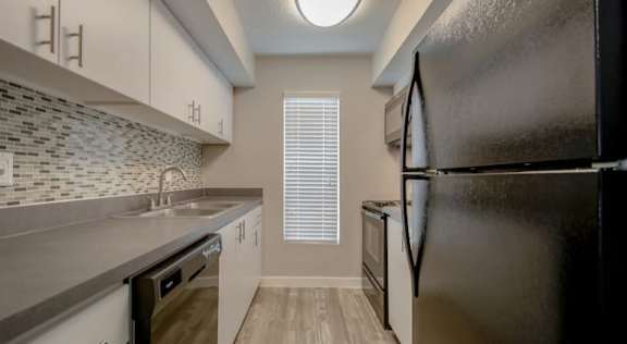 A kitchen with a black refrigerator, a sink, and a window with blinds. at Infinity on the Landing Apartments , Euless, Texas