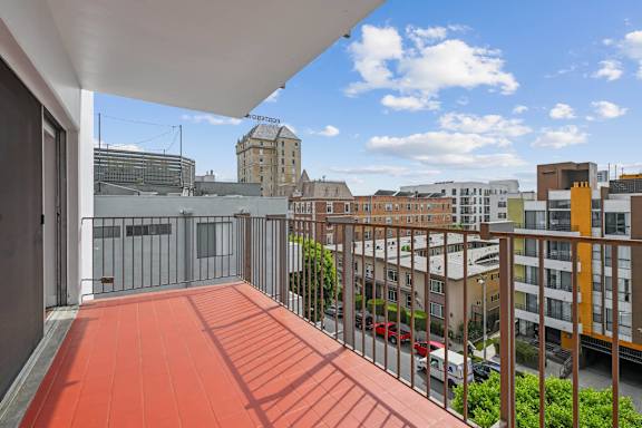 A balcony with a red floor and a metal railing overlooks a city street.