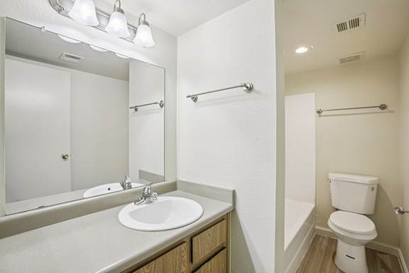 A white toilet is in a small bathroom with a sink and mirror.