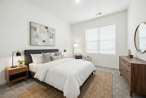 A bedroom with a large bed, a nightstand with a lamp, and a painting on the wall.