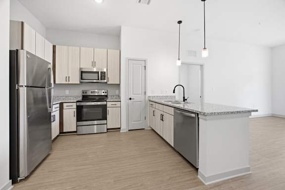 A kitchen with a refrigerator, microwave, oven, sink and cabinets.