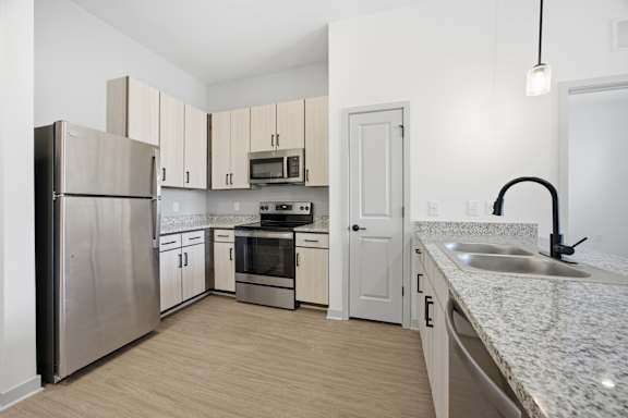 A kitchen with a refrigerator, oven, sink, and cabinets.