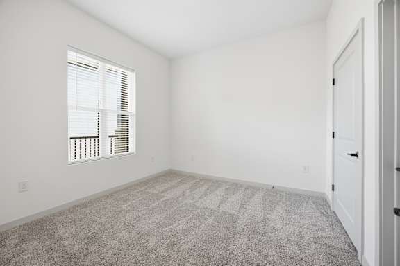 A room with a carpeted floor and a window with blinds.