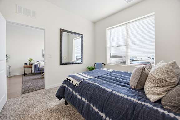 A bedroom with a bed, a mirror, and a window with blinds.