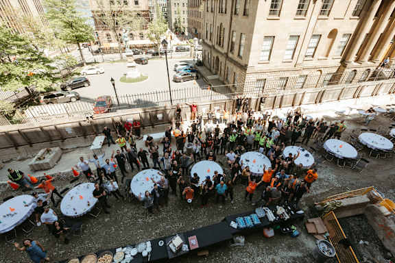 A large group of people are gathered around tables in an outdoor area.