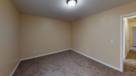an empty living room with carpet and a door to a bedroom