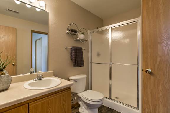A bathroom with a toilet, sink, and mirror. at Tranquility Pointe, Omaha