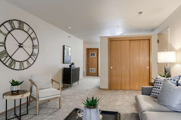 A living room with a large clock on the wall and a grey couch. at The Pointe, LaVista, Nebraska