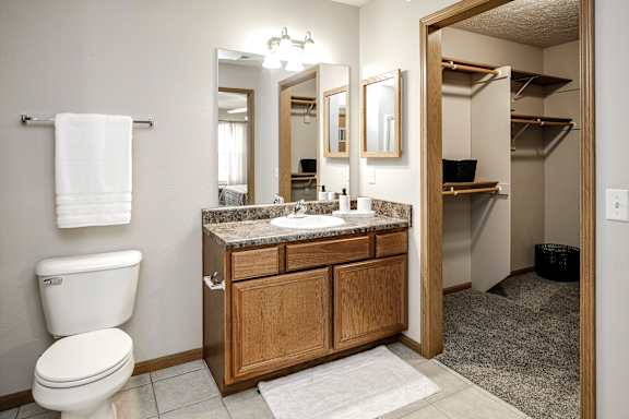 A bathroom with a toilet, sink, mirror and a white towel hanging on a towel rack. at Standing Bear Lake, Omaha, NE