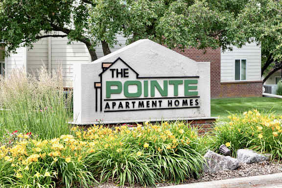 A sign for The Pointe Apartment Homes is surrounded by flowers.