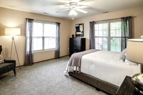 A bedroom with a large bed, a dresser, and a ceiling fan. at Tranquility Pointe, Omaha